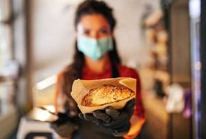 Food |Eine Person trägt eine Gesichtsmaske und hält ein Backwerk in einer Papiertüte.