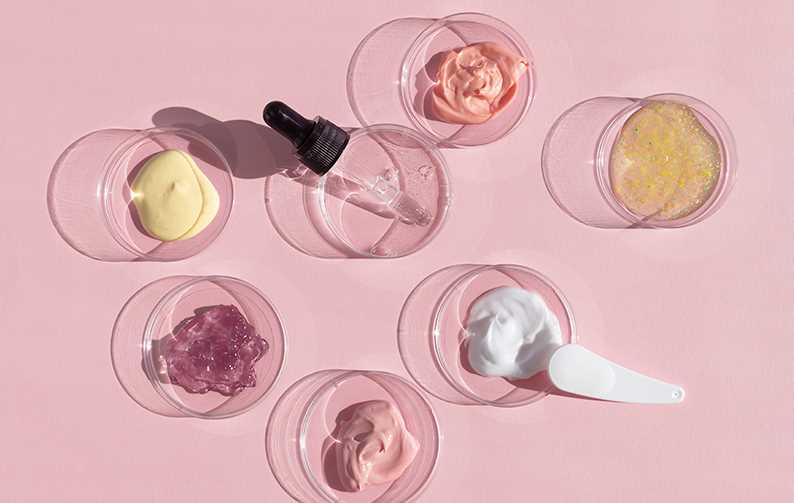 Multicolored texture of cream, scrub and gel with a pipette in a Petri dish on a pink background. The concept of laboratory research of cosmetics.