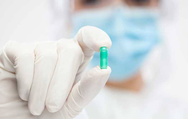 Female pharmacist wearing PPE personal protective equipment holding green pill