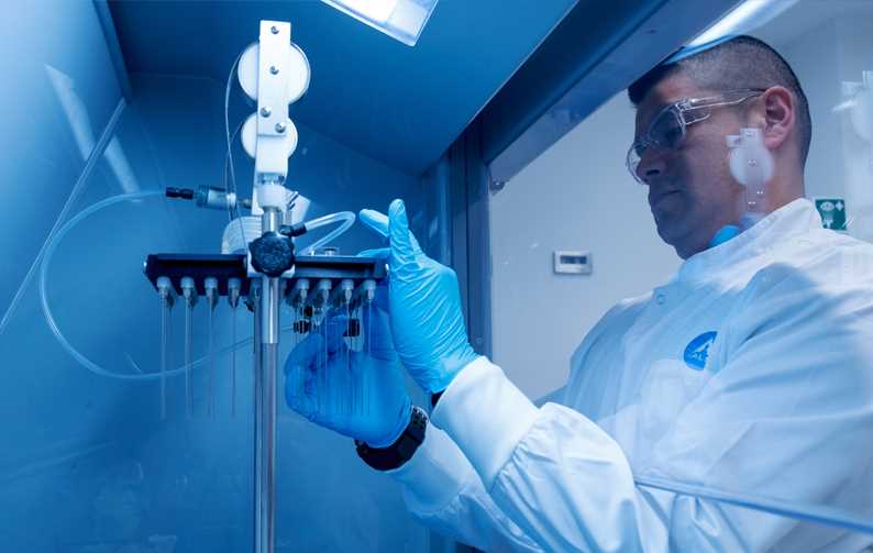 Lab technician adjusting aparatus in fume cuboard