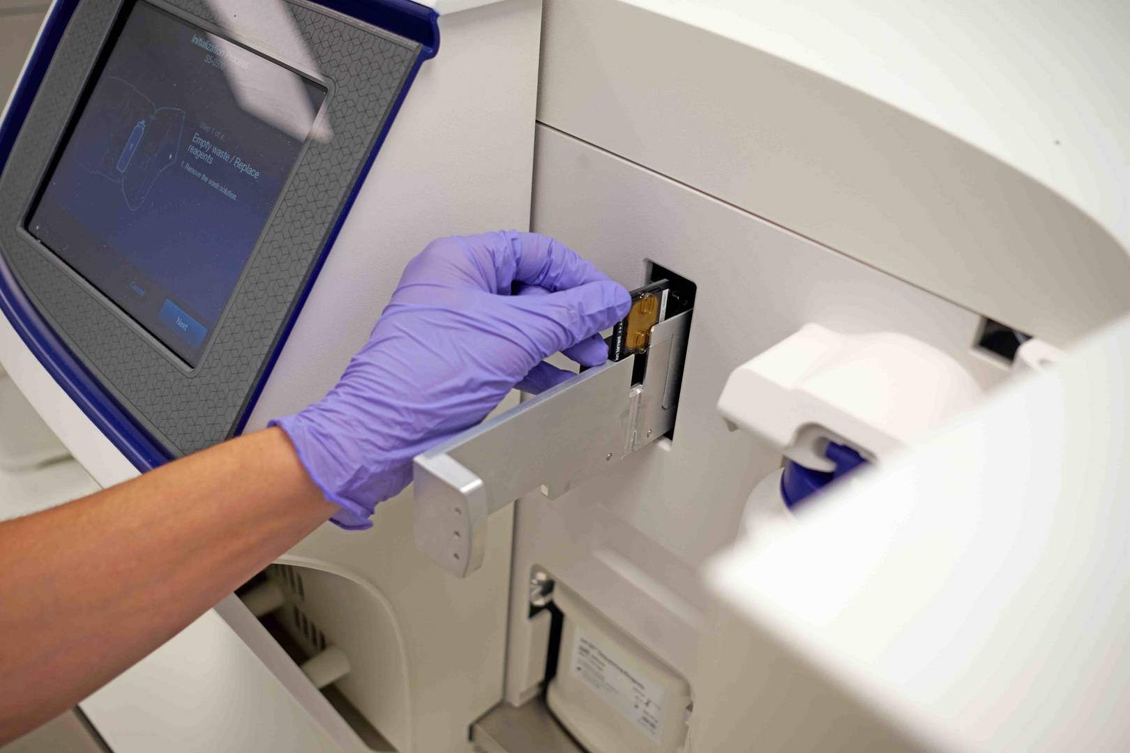 Pessoa com luvas roxas a operar um sequenciador NGS de DNA num laboratório.