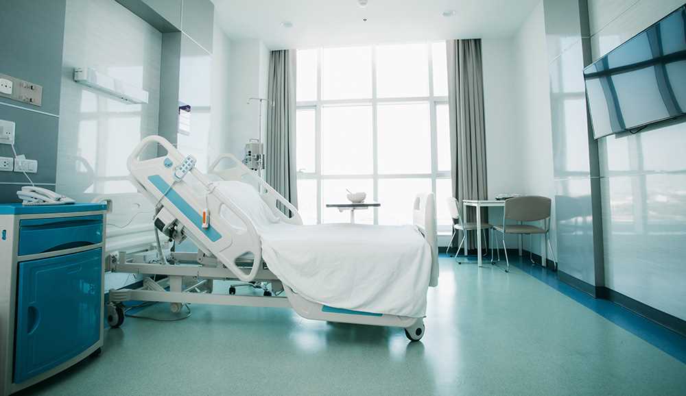 Quarto hospitalar moderno com cama articulada e equipamentos clínicos.