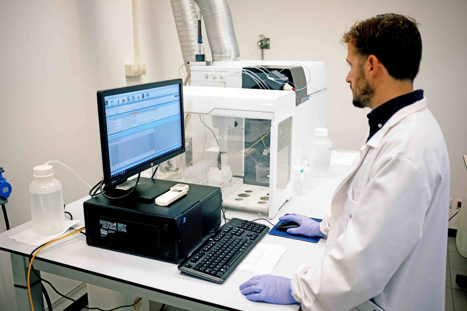 Peixes frescos empilhados numa caixa de plástico num mercado de peixe ao ar livre, com bancas e barcos ao fundo.