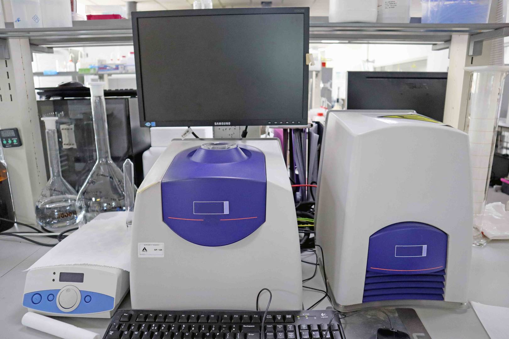 Setup laboratorial com equipamentos Oxford Instruments, incluindo MQC e dispositivos de análise, acompanhado por vidraria e computador