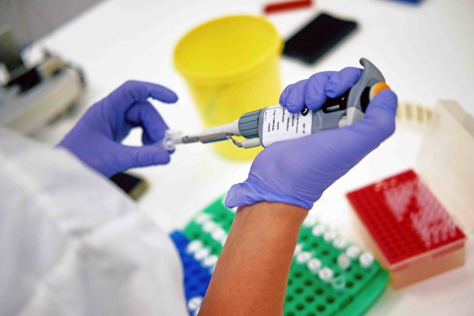 Técnico de laboratório usando pipeta para análise científica com equipamentos de teste ao fundo.