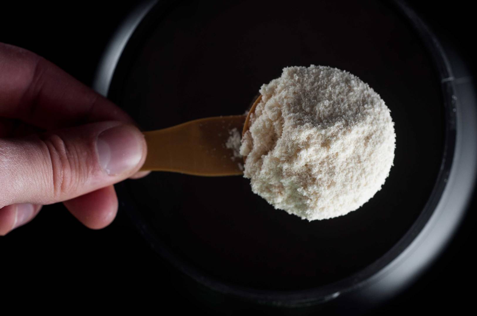 Pote de creatina em pó ao lado de uma colher medidora cheia, com o pó branco espalhado levemente sobre a mesa.