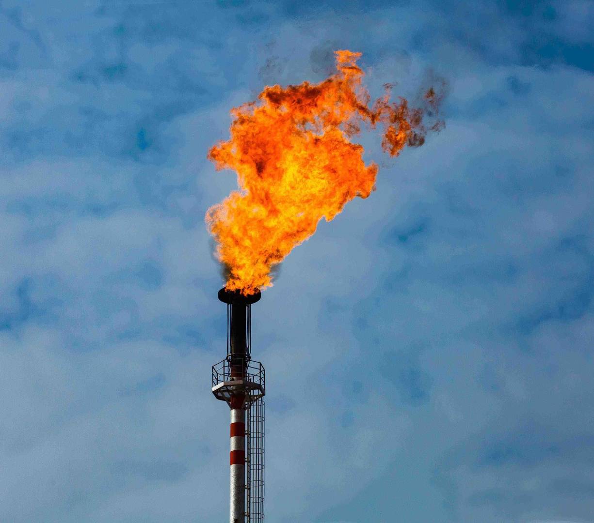 Mavi gökyüzü önünde duman yayan iki endüstriyel baca ve birinde koruyucu giysili bir kişi