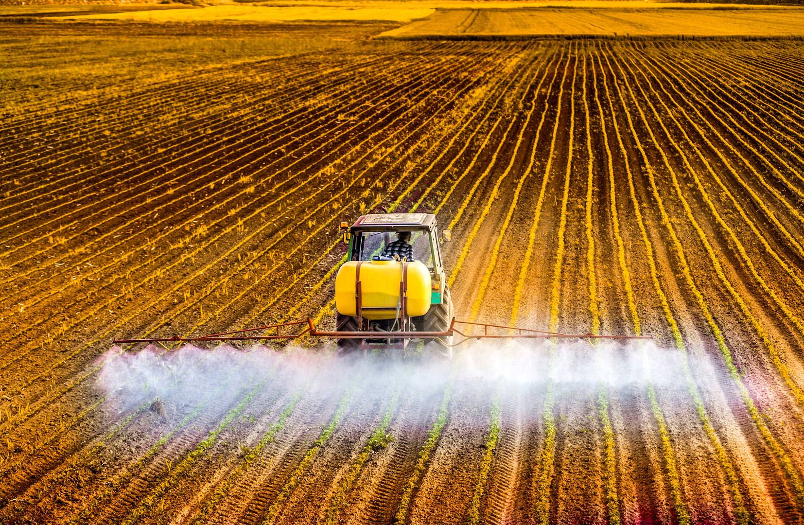 Traktor stříká pesticidy na poli