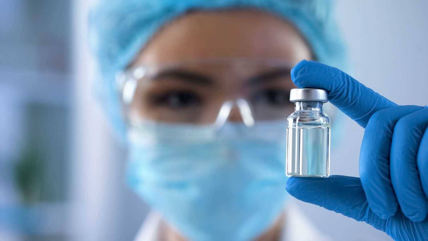 Laboratoriepersonal i skyddsutrustning håller upp ett provrör.