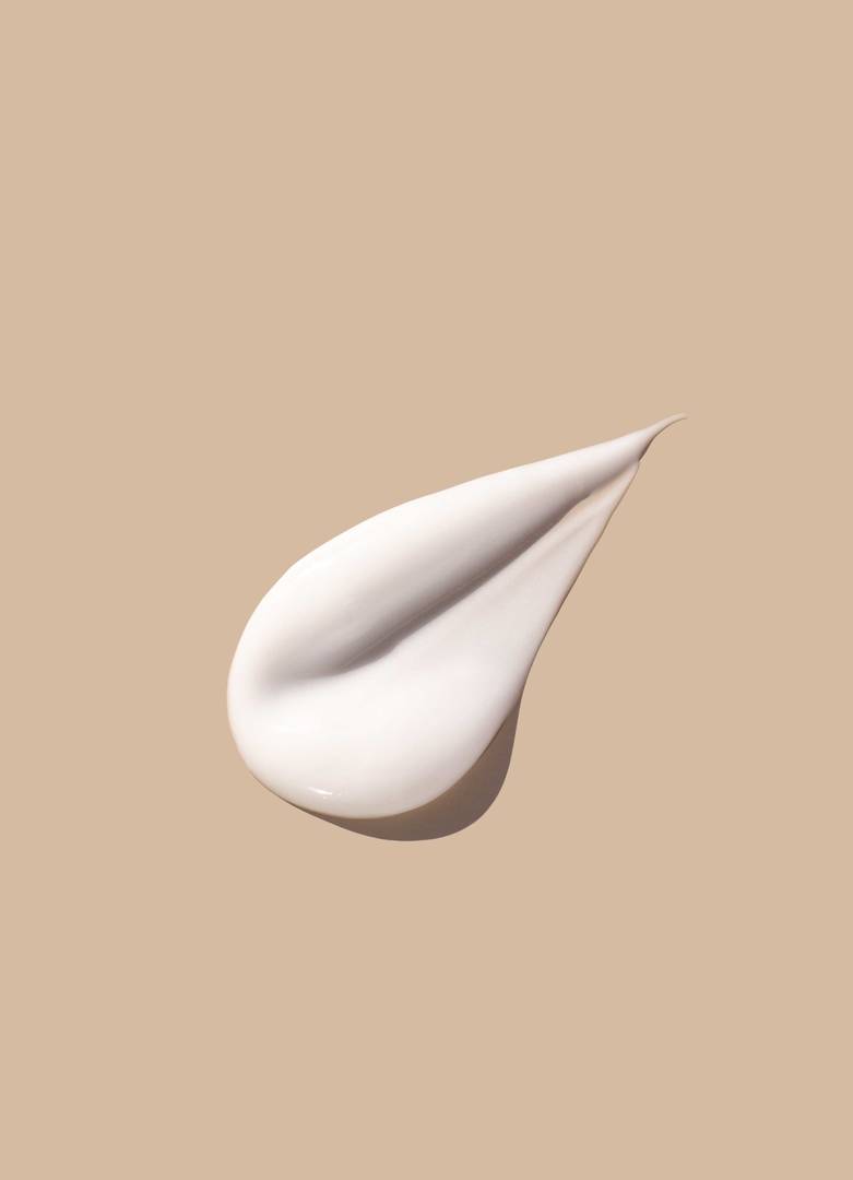 Närbild av en ljus hudkräm med silkeslen konsistens på beige bakgrund, kosmetisk produkt för hudvård och återfuktning.