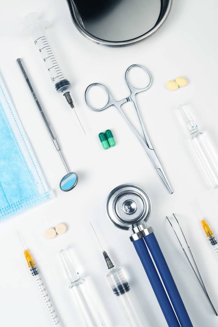 Medicinska instrument och läkemedel på vit bakgrund, inklusive sprutor, ampuller, stetoskop, kirurgiska verktyg och tabletter.