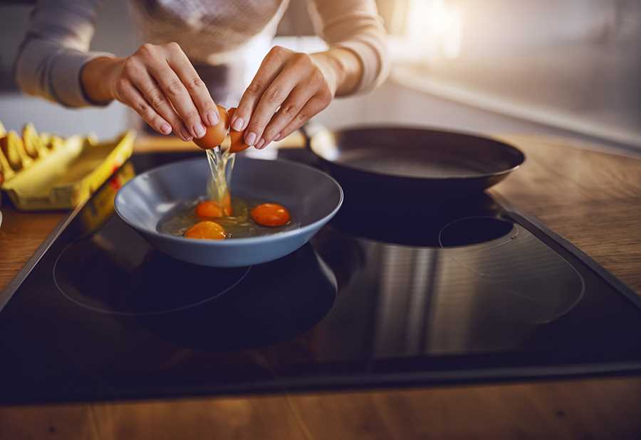 Pessoa a partir ovos para uma taça sobre um fogão de indução numa cozinha moderna.