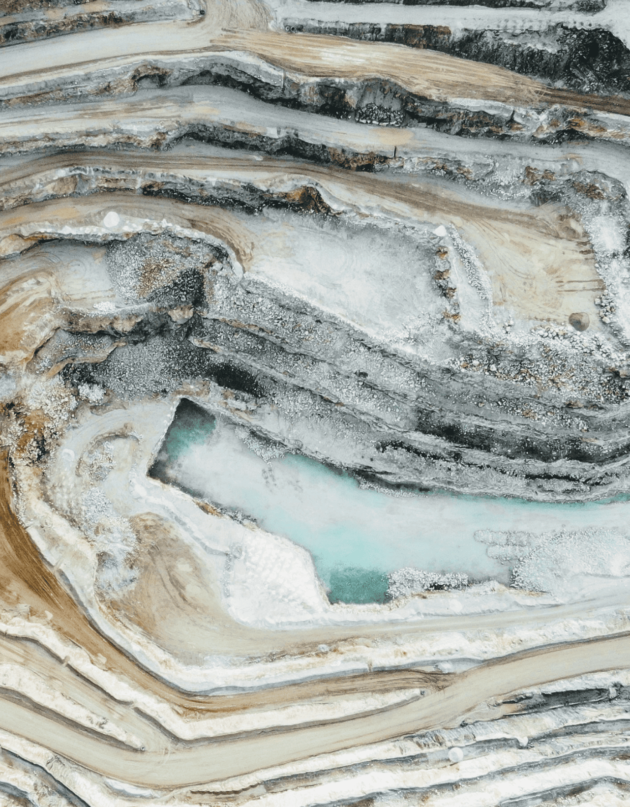 Aerial view of an open-pit mine with terraced benches and a turquoise pond